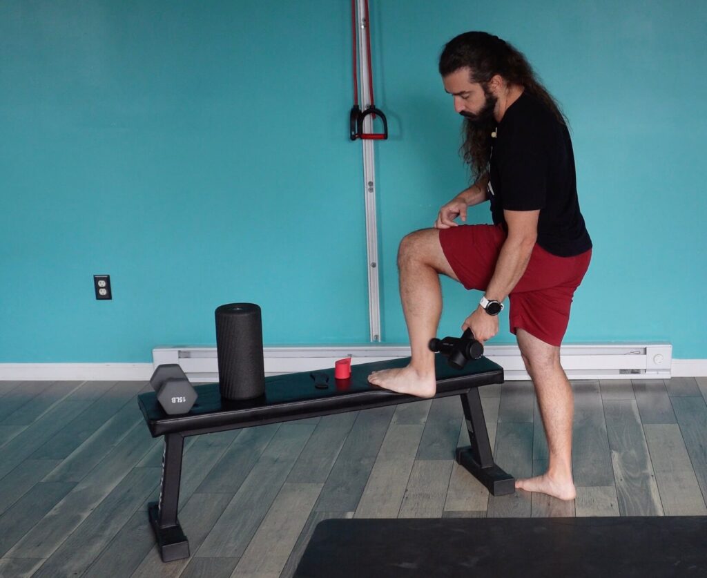 Dr. John with his foot on a bench to use his massage gun on the calf and achilles as a form of achilles tendinitis self-care